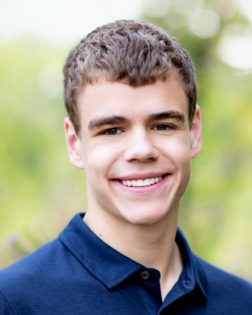 A photograph of Ben Weiner in a blue shirt against a blurred green natural background.